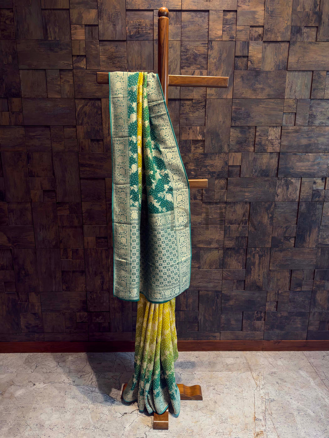 Green and yellow patterned blanket draped over a wooden cross against a textured wall.