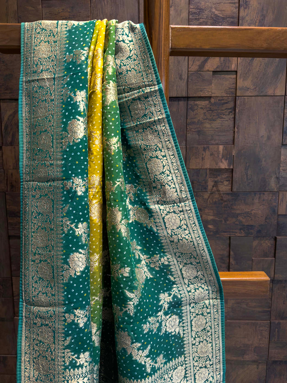 Green patterned fabric draped over a wooden chair against a wooden paneled wall.