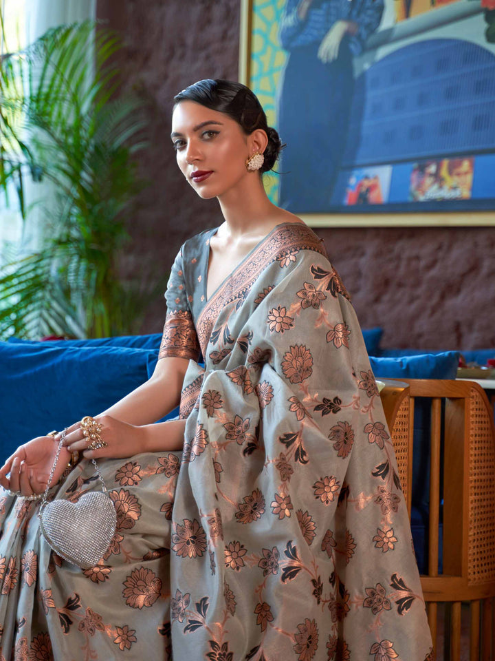 Elegant Grey Organza Saree adorned with Copper Zari Floral Patterns and a Rich Contrast Border, offering a Luxurious Drape—ideal for those seeking Authentic Ethnic Wear with a Contemporary Touch. 
