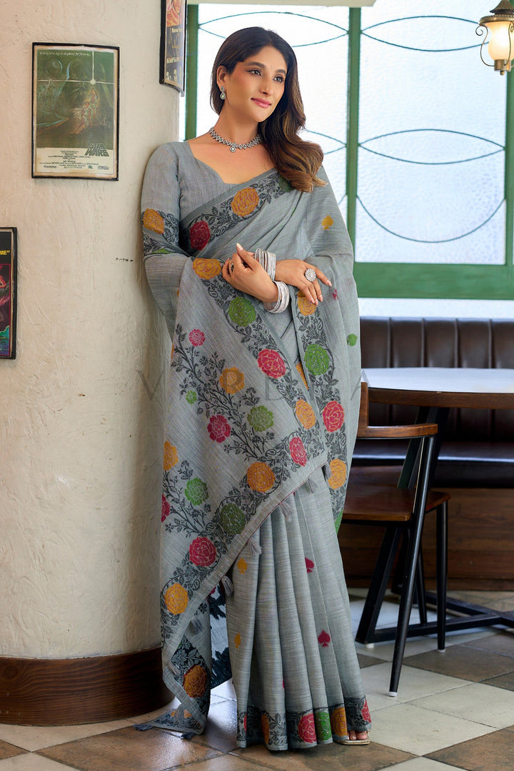 Woman posing gracefully in a grey linen party-wear saree, highlighting the beautiful fall, scattered body motifs, and traditional floral hem.