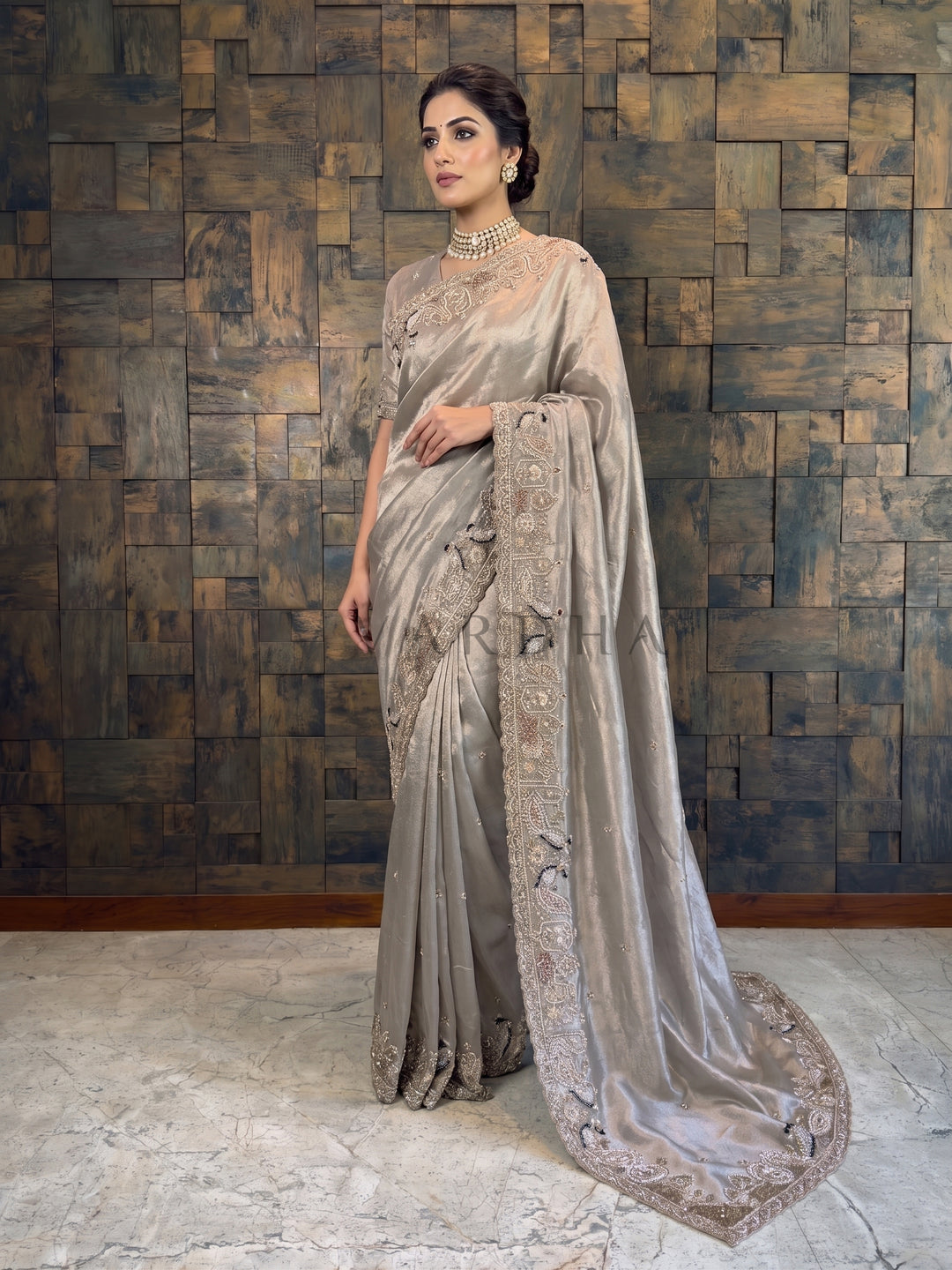 Woman in a saree standing against a textured wall.