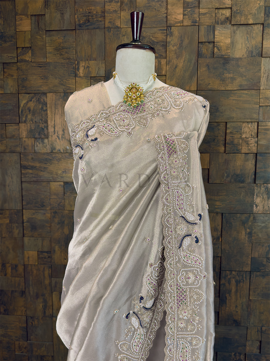 White saree with intricate embroidery on a mannequin against a wooden paneled wall. Close Up of Designer Cutdana and Pearl Border on Grey Tissue Saree, complete with custom stitched blouse with fall and edging.