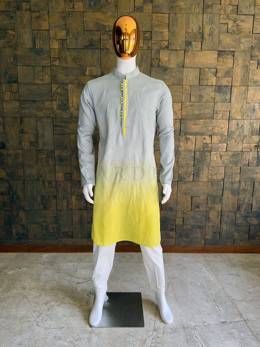 Mannequin wearing a gray to yellow gradient kurta against a wooden paneled wall. Front view of a man wearing a House of Vardha dual-tone grey and yellow viscose kurta featuring swirling topographical embroidery. Perfect men's ethnic wear for vibrant daytime festive events.