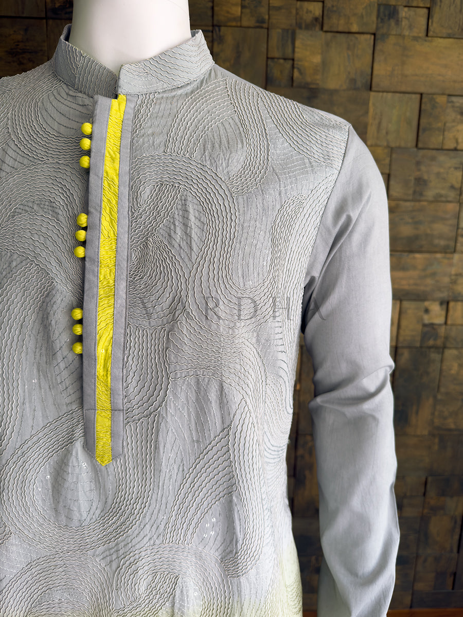 Gray embroidered kurta with yellow buttons on a mannequin against a wooden paneled wall. Close-up of the solid grey full sleeve contrasting with the vibrant yellow embroidered lower half of the premium viscose designer kurta for men.