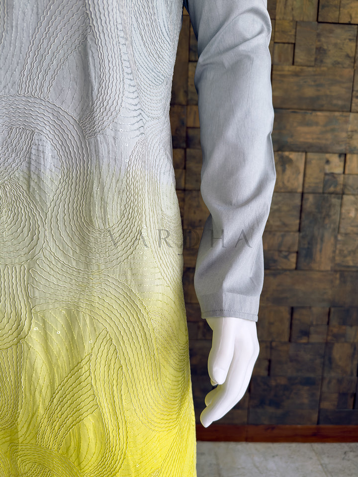 Mannequin wearing a long-sleeve shirt with a gradient design against a wooden paneled wall. Full-length view of the striking grey and yellow dual-tone designer kurta paired with white pyjama bottoms, showcasing the complete elegant silhouette for special occasions.