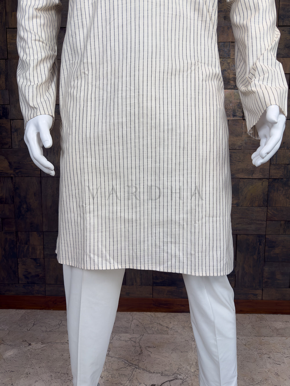Mannequin wearing a white pinstripe coat and pants against a wooden paneled wall.