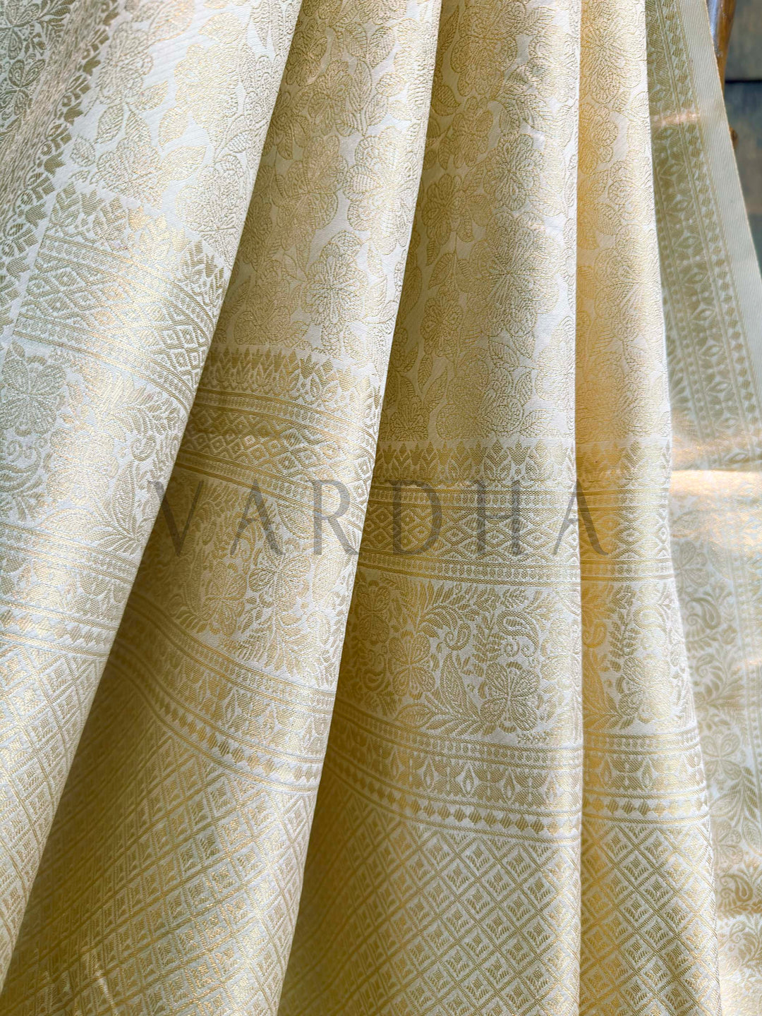 Angled pallu shot displaying heavy woven zari motifs—floral vines and geometric patterns—on champagne ivory art silk.