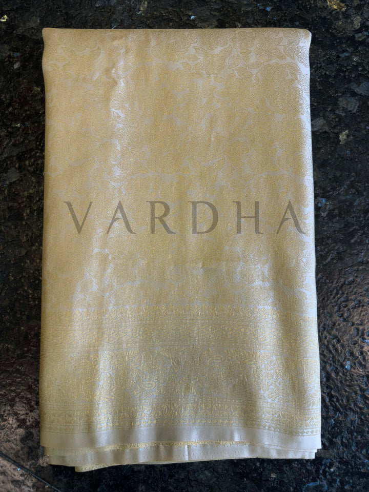 Macro detail of zari weave on ivory saree with continuous floral jaal and brocade transition, high-reflect finish.