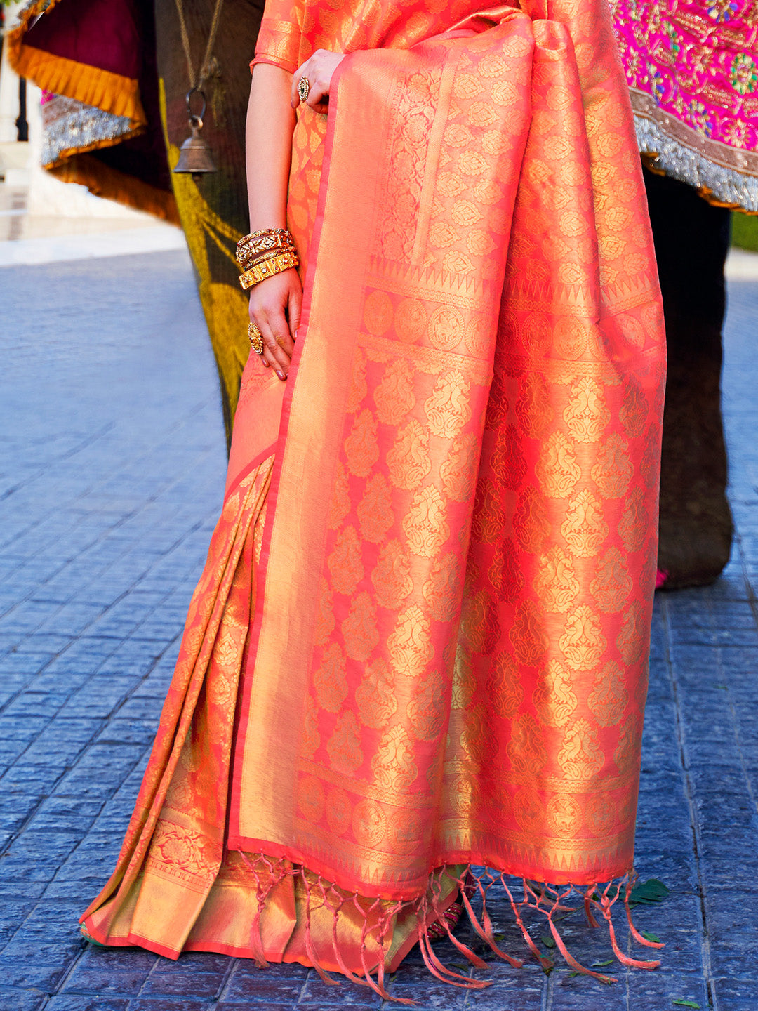 Golden woven kanjivaram drape with coral base perfect for traditional bridal functions. Coral kanjivaram silk saree featuring bridal motifs, zari border, and heavy pallu.