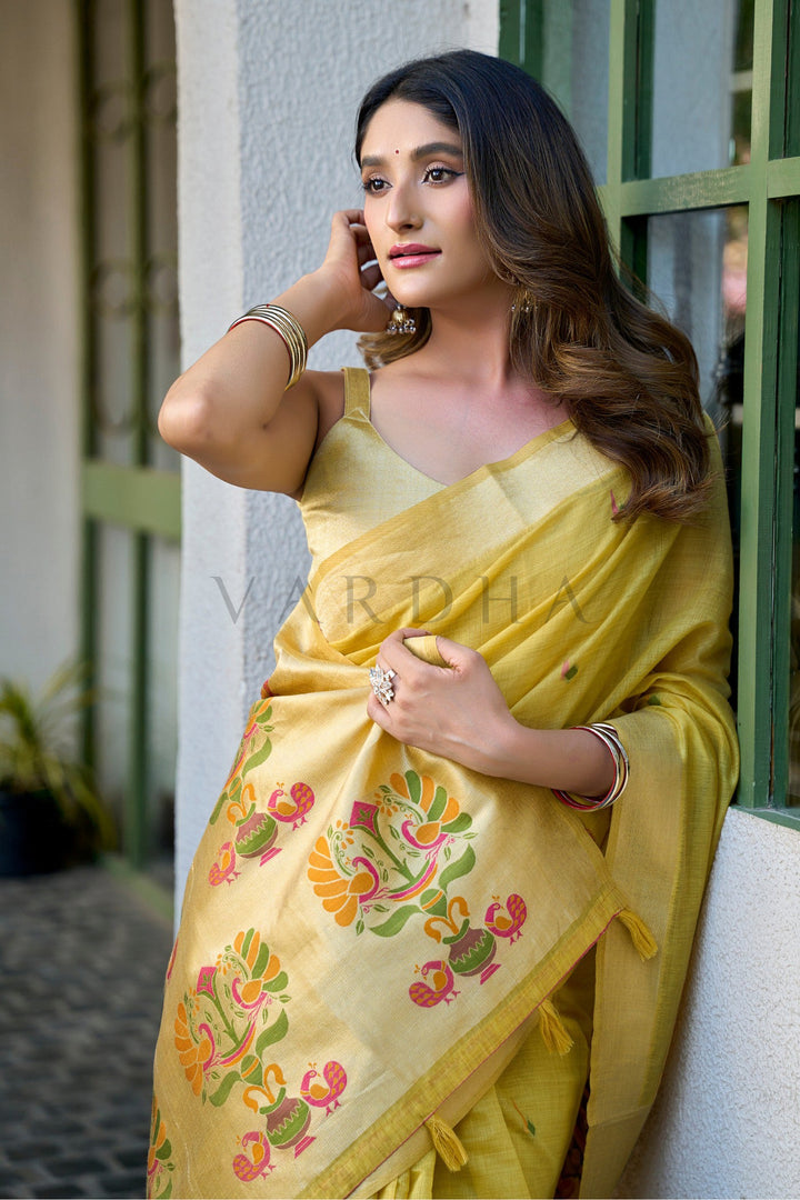 Woman wearing a yellow saree with floral patterns, standing against a light-colored wall. Graceful woman posing beautifully, highlighting the rich breathable texture, gleaming zari border, and regal festive appeal of the yellow cotton jacquard saree.