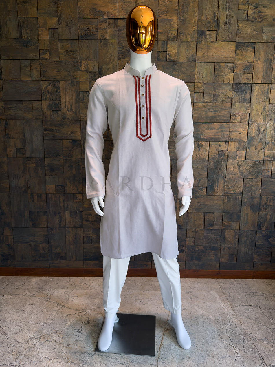 Mannequin wearing a grey kurta with red details against a wooden paneled wall. Front view of a man wearing a light grey cotton kurta featuring a bold maroon embroidered placket.
