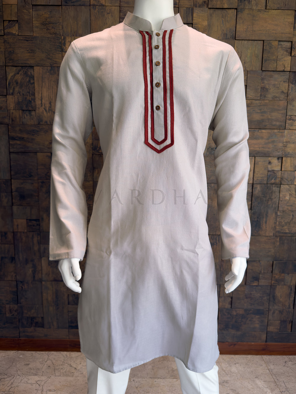 Grey kurta with red embroidery on a wooden background Close-up of the light grey kurta showing the geometric maroon embroidery framing the button placket and mandarin collar.
