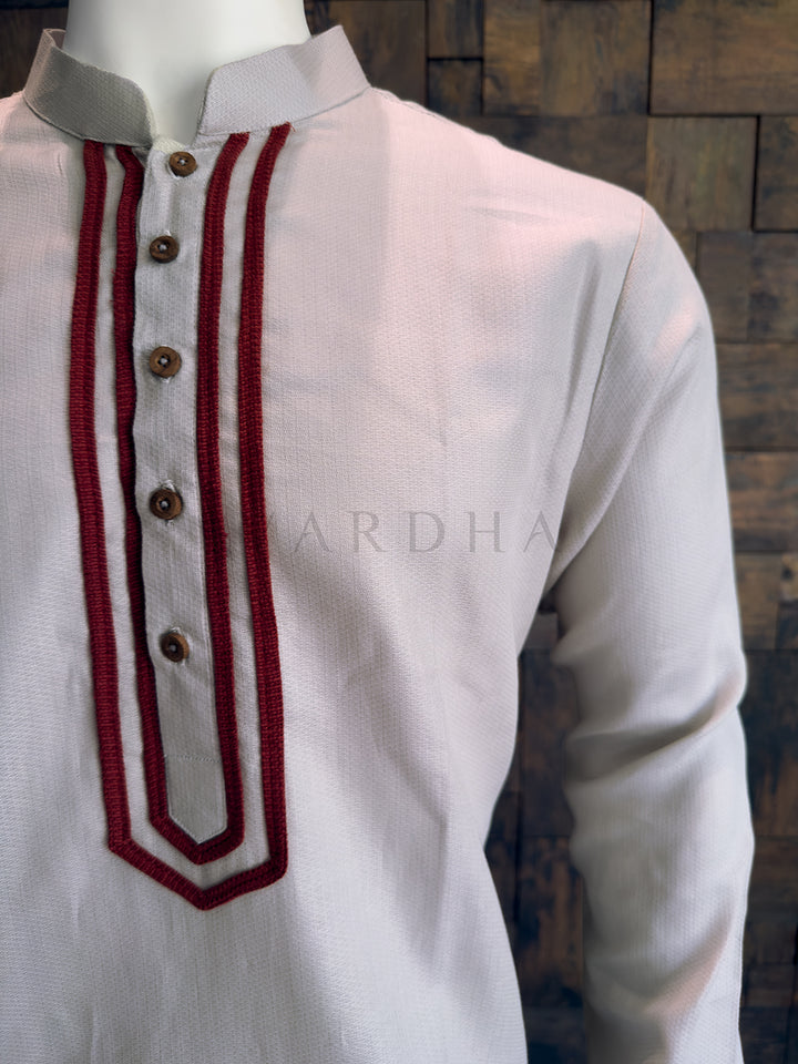 Grey kurta with red embroidery on a wooden background Side profile of the light grey minimalist cotton kurta for men, highlighting the crisp drape and clean lines.