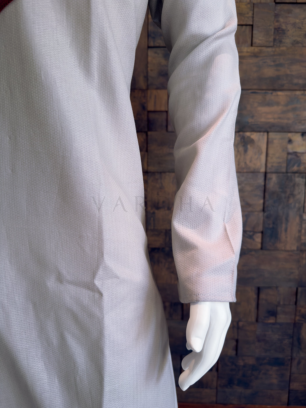 Grey kurta on a mannequin against a wooden paneled Close-up of the full sleeve and subtle woven texture on the light grey cotton fabric. 