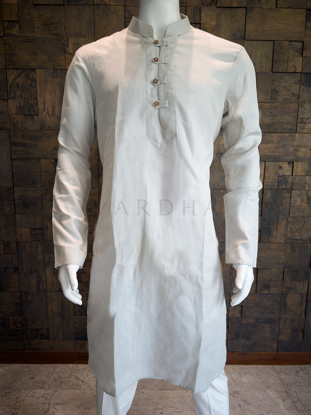 grey kurta on a mannequin against a wooden paneled wall. Premium Light Grey cotton kurta highlighting the breathable micro-textured fabric and meticulous artisanal tailoring for a refined silhouette.