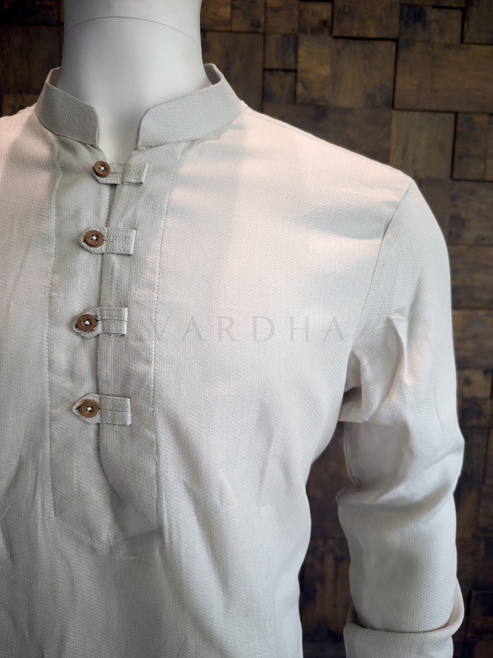 Light-colored shirt on a mannequin with a wooden background. Versatile Light Grey cotton kurta with rustic detailing; an ideal ethnic ensemble when paired with white or cream pyjamas.