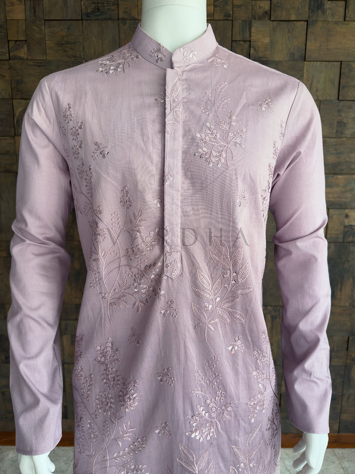 Light purple embroidered shirt on a mannequin against a wooden paneled wall. Detailed chest view of the embroidered mandarin collar and the elegant floral sequin patterns on the light lilac designer kurta for men. High-quality ethnic party wear.