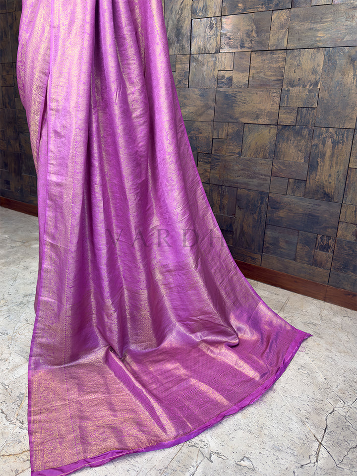 Purple fabric draped over a textured wall. Close-up view of the House of Vardha Lilac Kanjivaram Silk Saree highlighting the detailed Gold Zari Weave on the pleats and pallu. We offer Ready to wear, Pre drape service, Saree Add on, Custom Stitched Blouse, Fall and Edging, Gift Packaging at Complimentary Price!