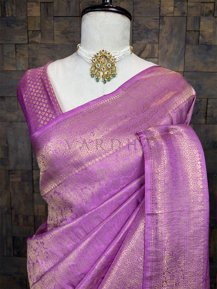 Purple saree with gold patterns on a mannequin against a wooden paneled wall. House of Vardha designer Lilac Kanjivaram Silk Saree featuring a traditional Gold Zari Weave across the body and a decorative, heavy border. We offer Ready to wear, Pre drape service, Saree Add on, Custom Stitched Blouse, Fall and Edging, Gift Packaging at Complimentary Price!