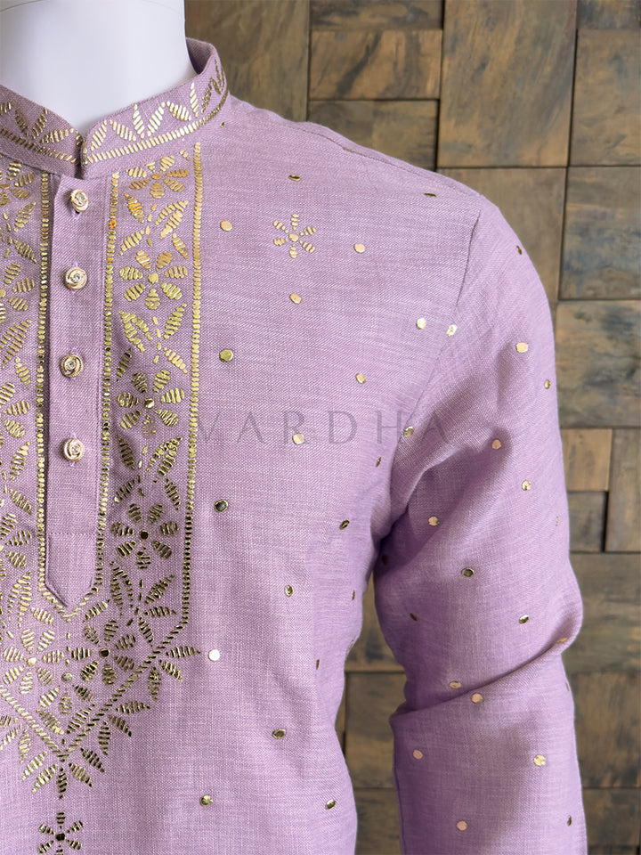 Elegant lilac khadi kurta with gold mukaish detailing and mandarin collar ethnic outfit embroidered shirt with gold details on a mannequin against a wooden paneled wall.