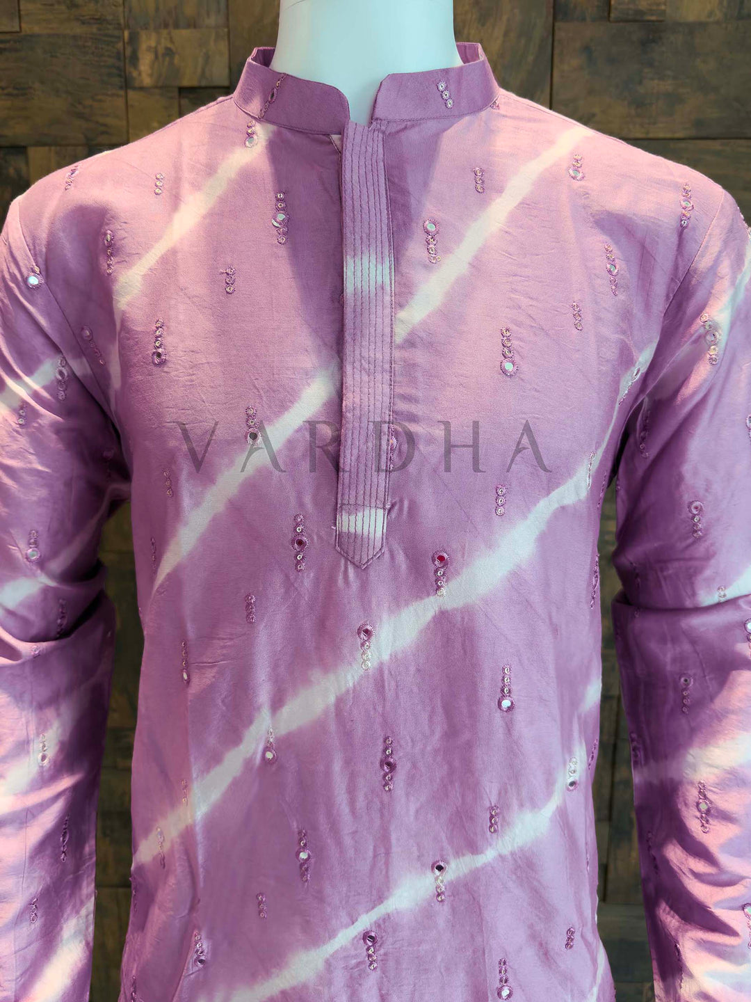 Purple kurta with white patterns on a mannequin against a wooden panel background Purple kurta with white patterns on a mannequin against a wooden panel background Close-up of lilac kurta neckline showing clean band collar and pintucked concealed placket with delicate sequin clusters on smooth viscose fabric.
