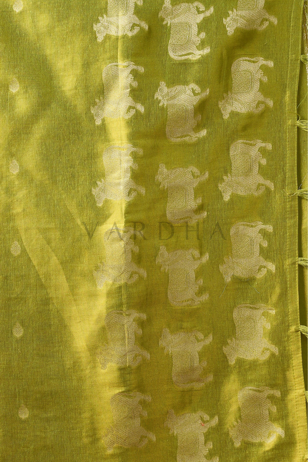 Close-up of a yellow fabric with a subtle pattern on a green background Detailed fabric close-up of the green heavy tissue saree showcasing the intricate silver zari woven cow (Pichwai) buttas and fancy tassels.