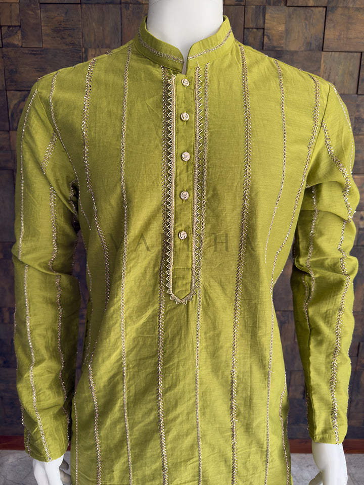 Green kurta with intricate patterns on a wooden background. Detailed chest view highlighting the premium jeweled buttons and the sharp zigzag metallic embroidery framing the placket on the lime green designer kurta for men.