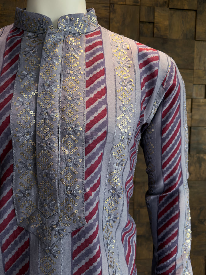 Mannequin wearing a traditional embroidered garment with red, white, and blue stripes against a wooden panel background.