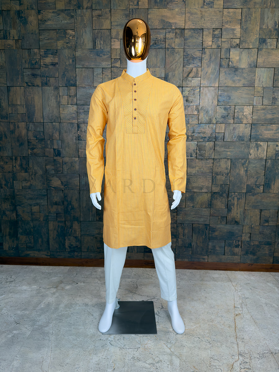 Mannequin wearing a yellow kurta with white pants against a textured wall.