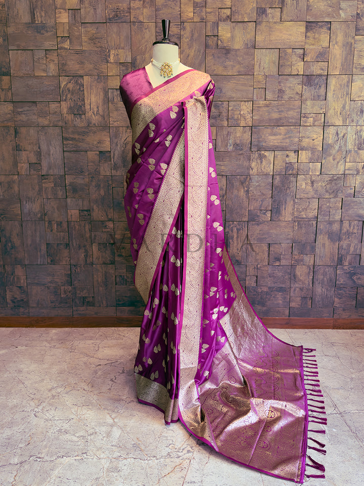 Purple saree with gold patterns on a mannequin against a wooden paneled wall. Full front view of a magenta purple satin silk saree draped elegantly on a mannequin showcasing gold zari bootis.