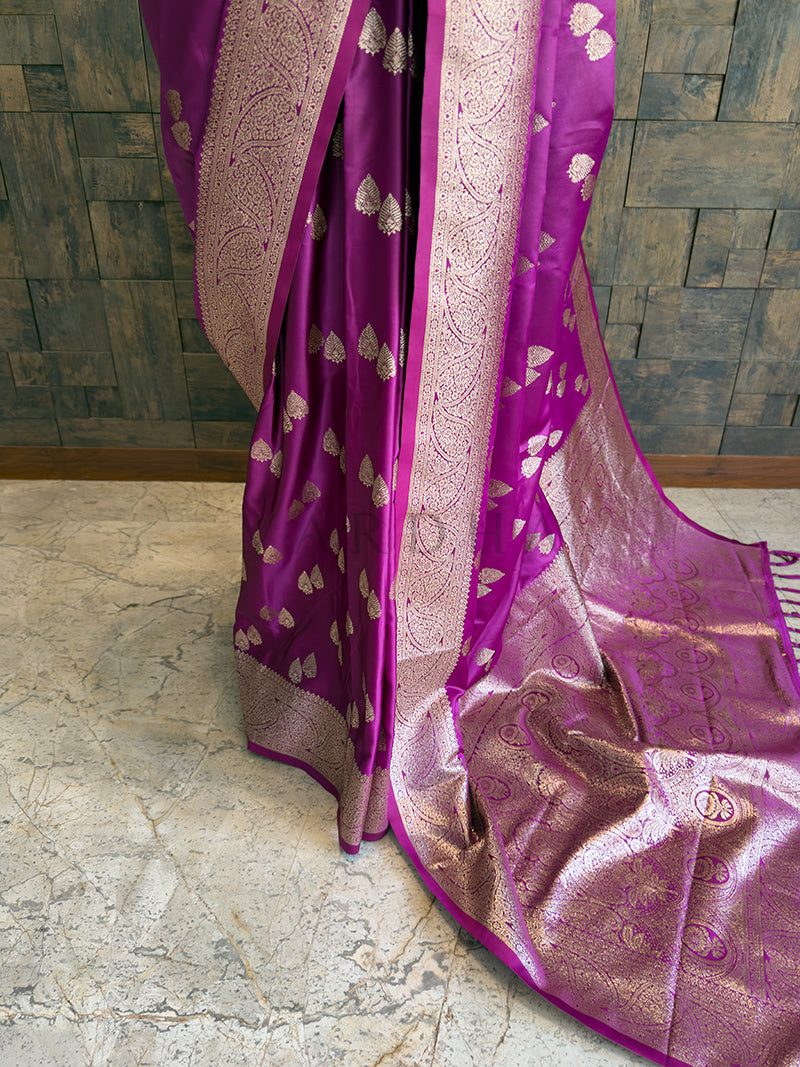 Purple saree with gold patterns on a stone floor and tiled wall background Traditional magenta purple woven satin saree styled on a mannequin display paired with a pearl and emerald choker necklace.