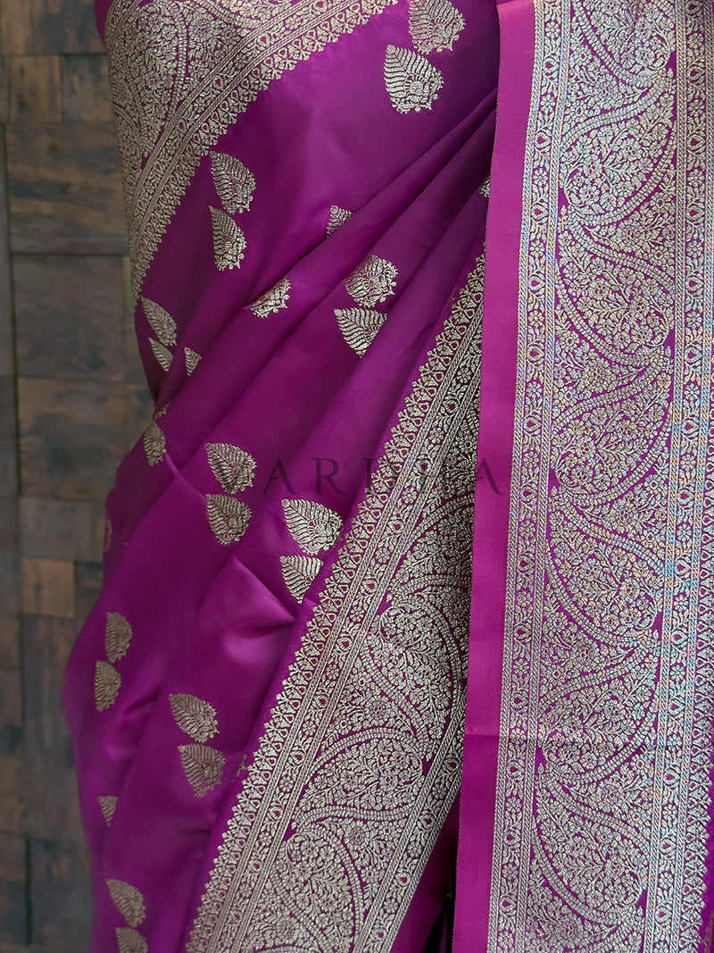 Purple saree with silver leaf patterns on a textured wall background  Detailed floor view of the heavy paisley zari woven pallu with delicate tassels on the deep purple saree.