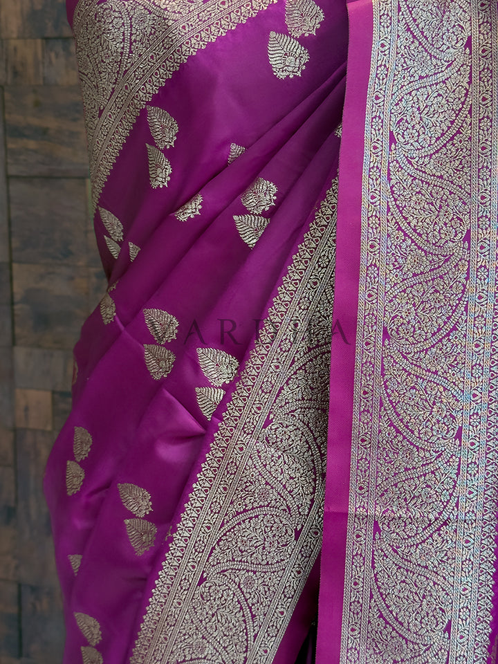 Purple saree with silver leaf patterns on a textured wall background  Detailed floor view of the heavy paisley zari woven pallu with delicate tassels on the deep purple saree.