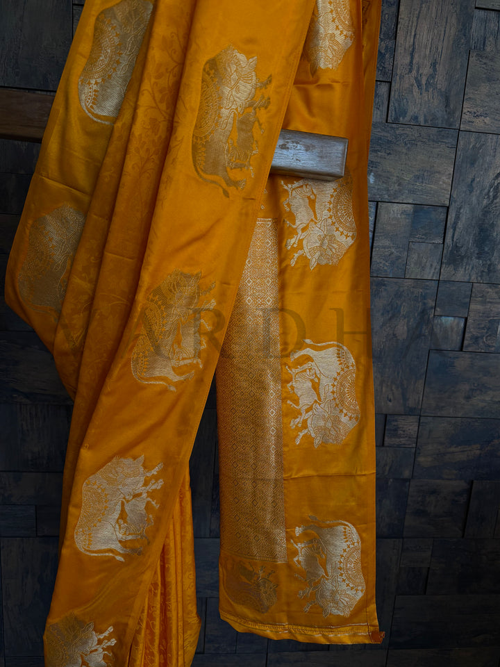 Festive satin saree in deep orange hue with intricate zari woven elephant pattern.

Elegant mustard-orange satin saree with traditional elephant design and silky finish.

