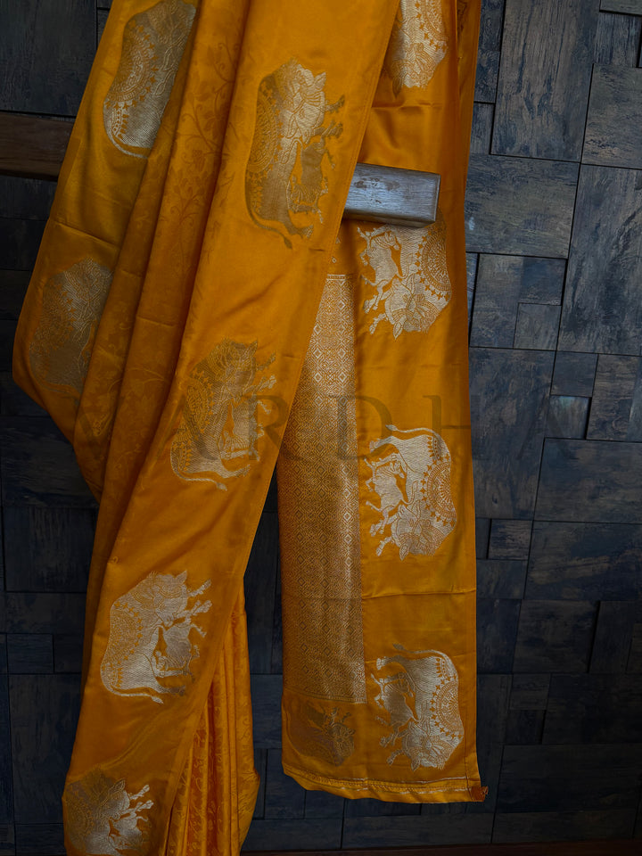 Women’s partywear satin saree in mustard orange with golden woven detailing.


