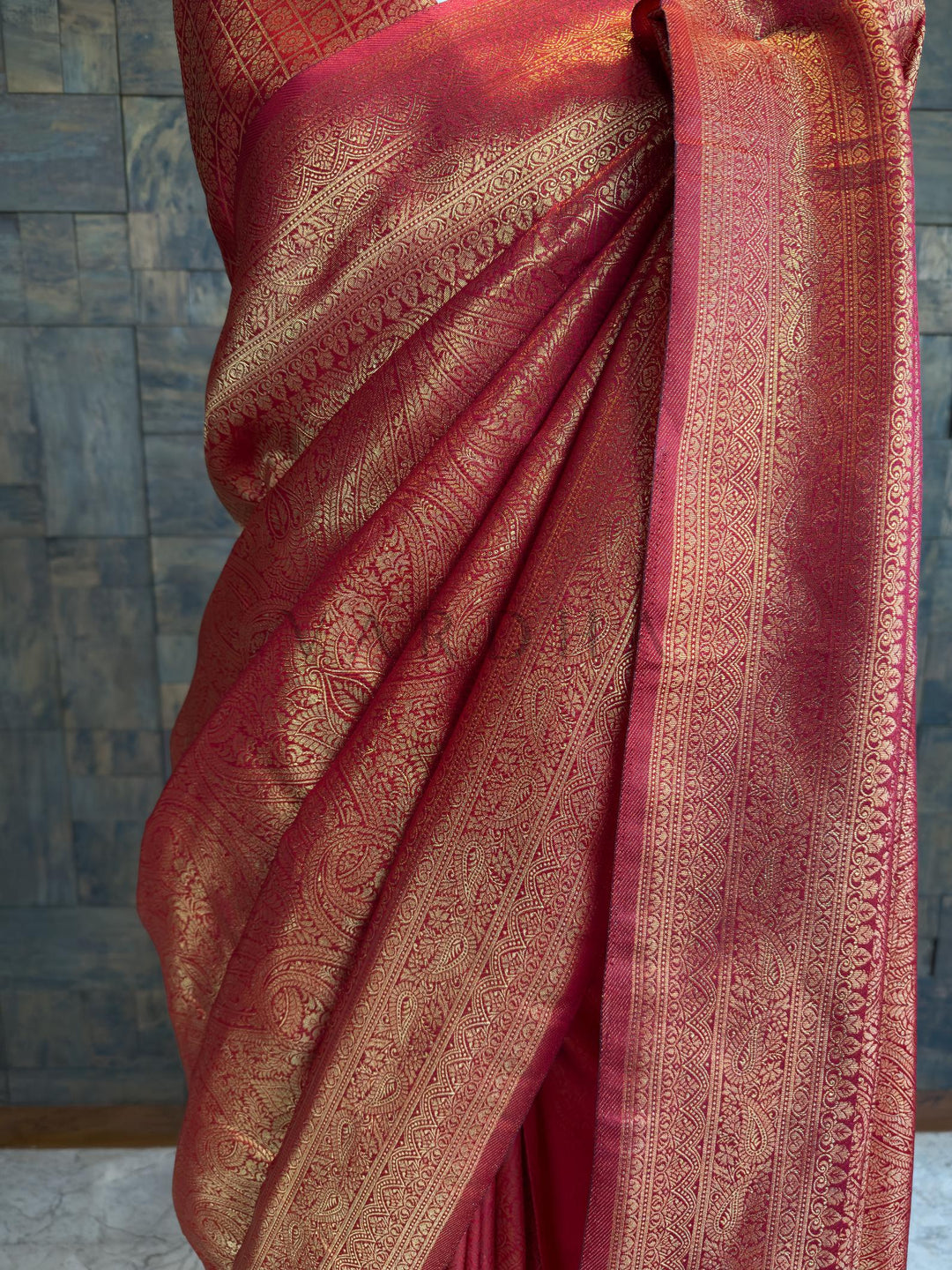 Maroon saree with gold patterns draped over a textured surface. House of Vardha deep Maroon festive saree detailed with elaborate gold zari floral and geometric weaving along the pallu and border.