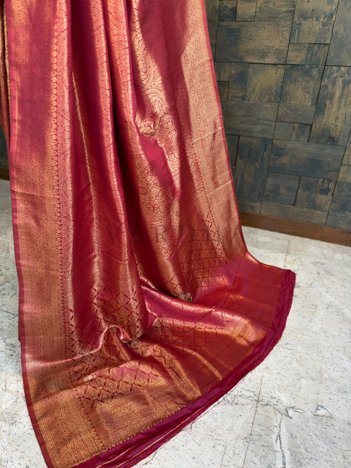 Maroon saree with gold patterns on a wooden floor. Traditional maroon Indian saree with extensive gold zari embellishments and matching border, beautifully draped by House of Vardha.
