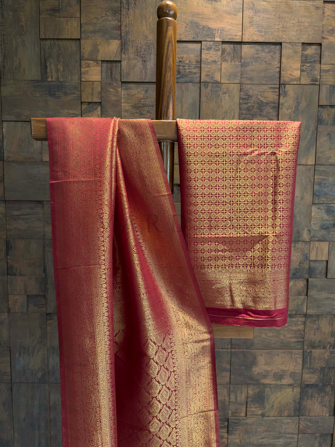 Maroon Golden Zari Kanjivaram Silk Saree House of Vardha. House of Vardha exclusive red and gold woven silk saree with heavy zari pallu and traditional border draped against a textured wall.