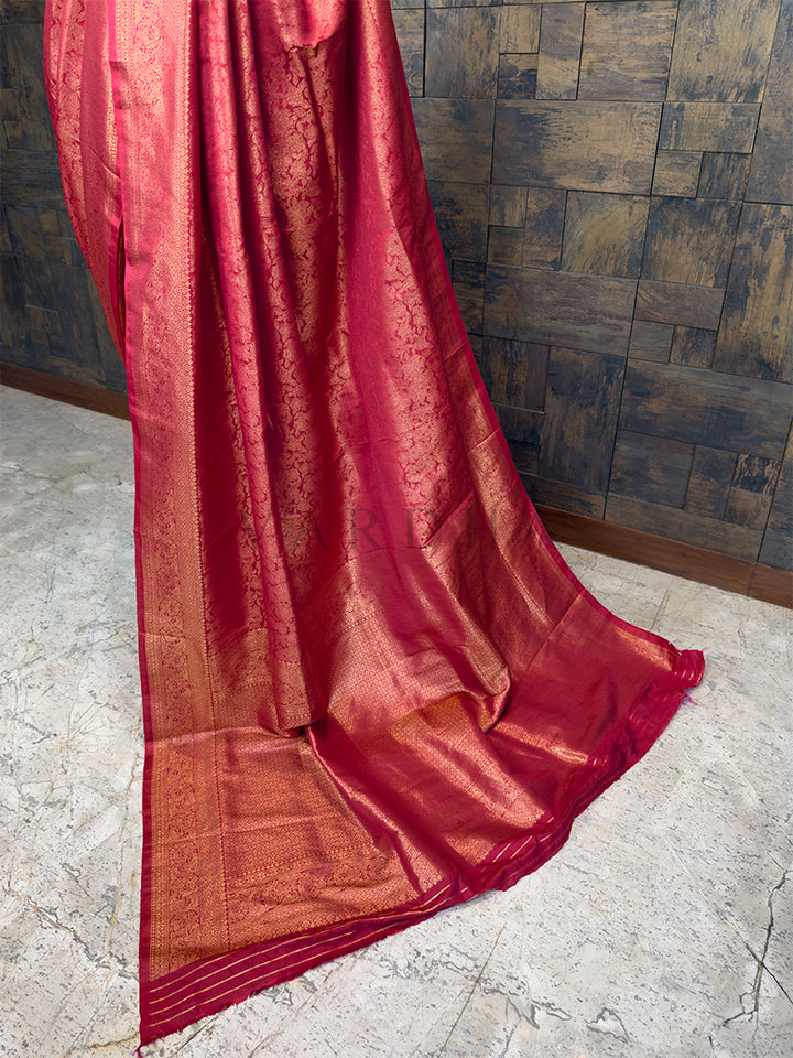 Maroon saree with gold patterns on a stone floor and wooden wall background. Luxurious Indian bridal saree in a deep red tone from House of Vardha with heavy gold zari embellishments. We offer Ready to wear, Pre drape service, Saree Add on, Custom Stitched Blouse, Fall and Edging, Gift Packaging at Complimentary Price!