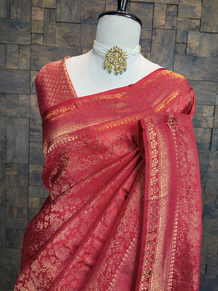 Red saree with gold patterns on a mannequin against a textured wall background. Elegant copper-red festive saree by House of Vardha featuring intricate traditional gold woven floral motifs. We offer Ready to wear, Pre drape service, Saree Add on, Custom Stitched Blouse, Fall and Edging, Gift Packaging at Complimentary Price!