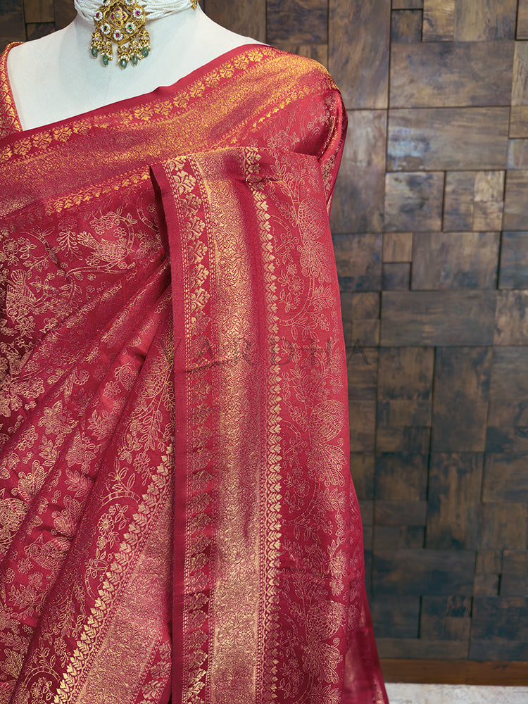 Red saree with gold patterns on a mannequin against a wooden paneled wall. Luxurious Indian bridal saree in a deep pink-red tone from House of Vardha with heavy gold zari embellishments. We offer Ready to wear, Pre drape service, Saree Add on, Custom Stitched Blouse, Fall and Edging, Gift Packaging at Complimentary Price!