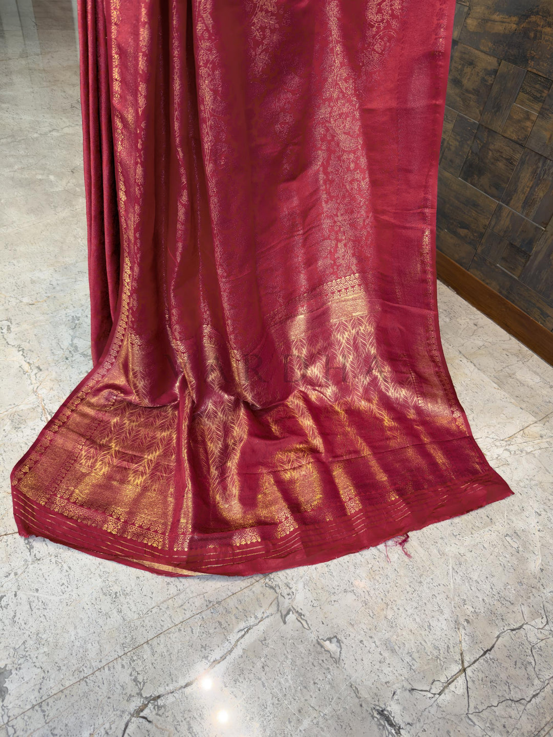 Red saree with gold patterns on a marble floor Luxurious Indian bridal saree in a deep pink-red tone from House of Vardha with heavy gold zari embellishments. We offer Ready to wear, Pre drape service, Saree Add on, Custom Stitched Blouse, Fall and Edging, Gift Packaging at Complimentary Price!