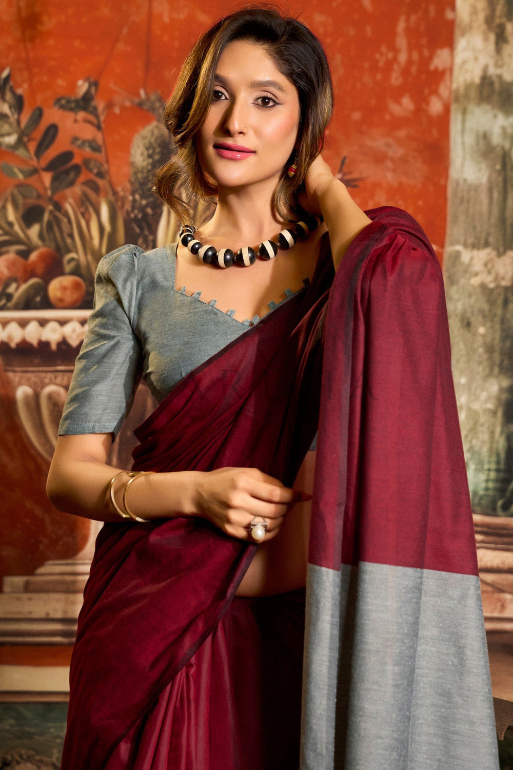 Woman in a maroon and gray saree with a decorative background Beautiful woman posing gracefully in a soft maroon mal cotton saree with a grey contrast blouse, perfect for summer office wear.