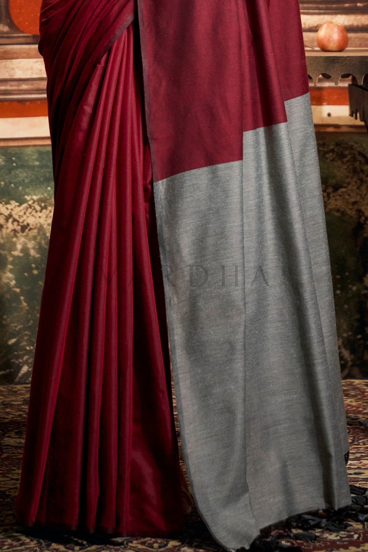 Maroon and gray saree draped over a chair with a blurred background Detailed fabric close-up of the maroon mal cotton saree highlighting the perfectly pleated texture and the solid grey contrast pallu edge.