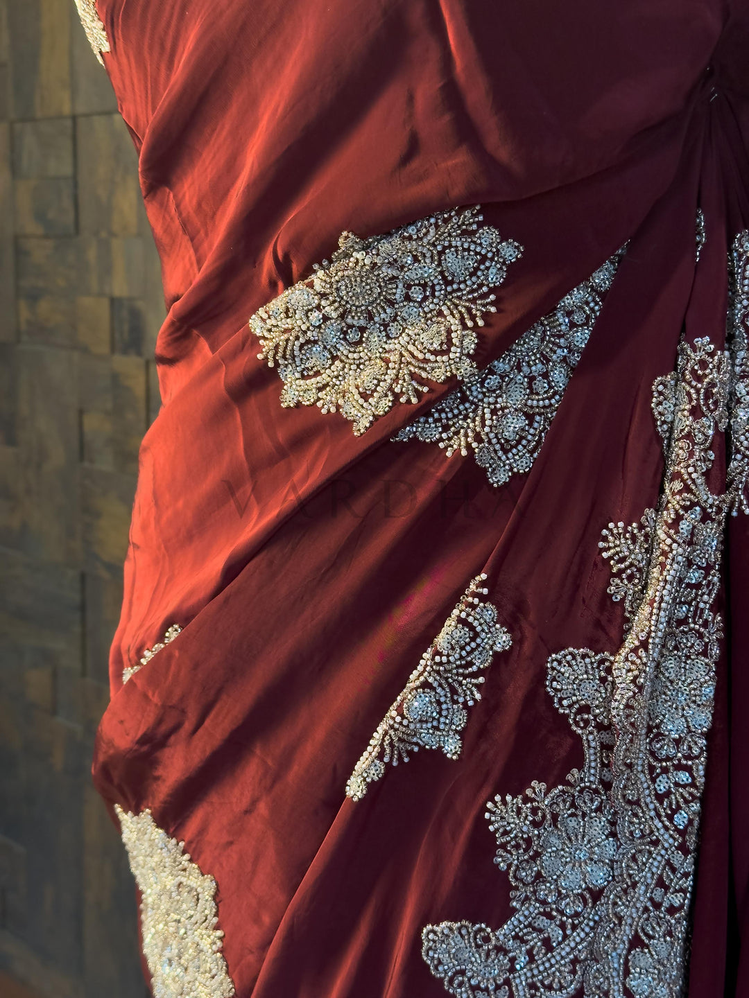 Macro Detail of Cutdana and Zircon Embroidery on Wine Red Fabric. Beautifully draped Maroon Satin Crepe Saree highlighting the smooth fall of the fabric and shimmering Silver Cutdana handwork from House of Vardha. We offer Ready to wear, Pre drape service, Saree Add on, Custom Stitched Blouse, Fall and Edging, Gift Packaging at Complimentary Price!