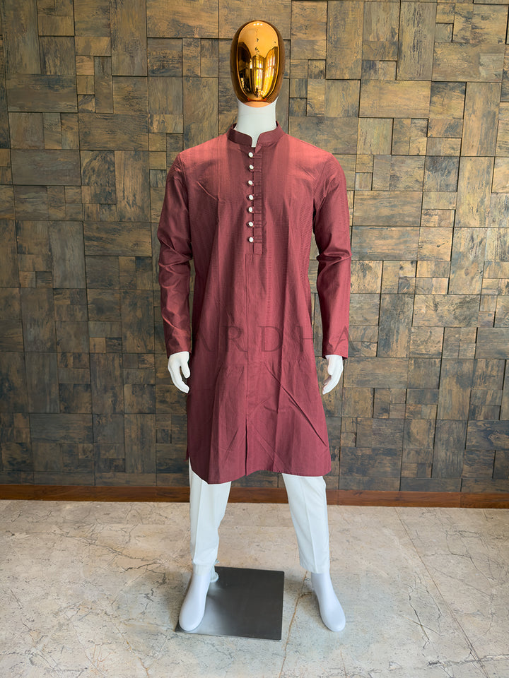 Maroon kurta on a mannequin against a wooden paneled wall. Regal Maroon knee-length kurta with sharp architectural tailoring, a Mandarin collar, and full sleeves ideal for evening weddings and formal receptions.