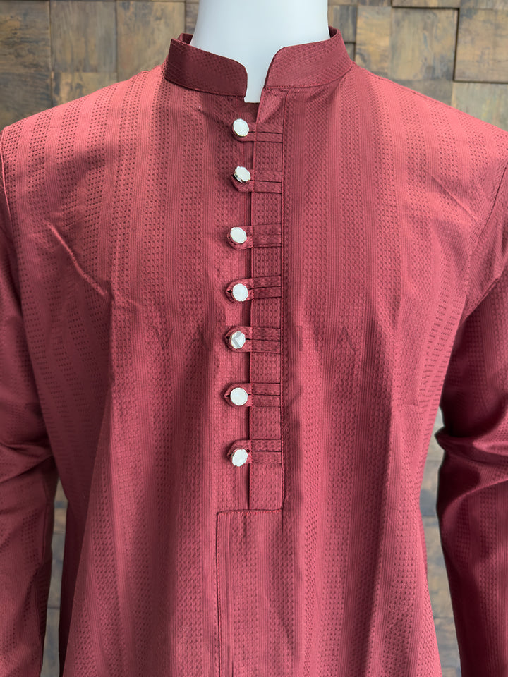 Maroon kurta with white buttons on a wooden background. Close-up of a designer burgundy kurta showing an extended chest placket with traditional fabric loops and striking metallic silver mirror-finish buttons.