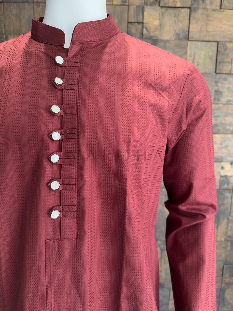 Maroon kurta with white buttons on a mannequin against a wooden paneled wall. A minimalist yet luxurious men&