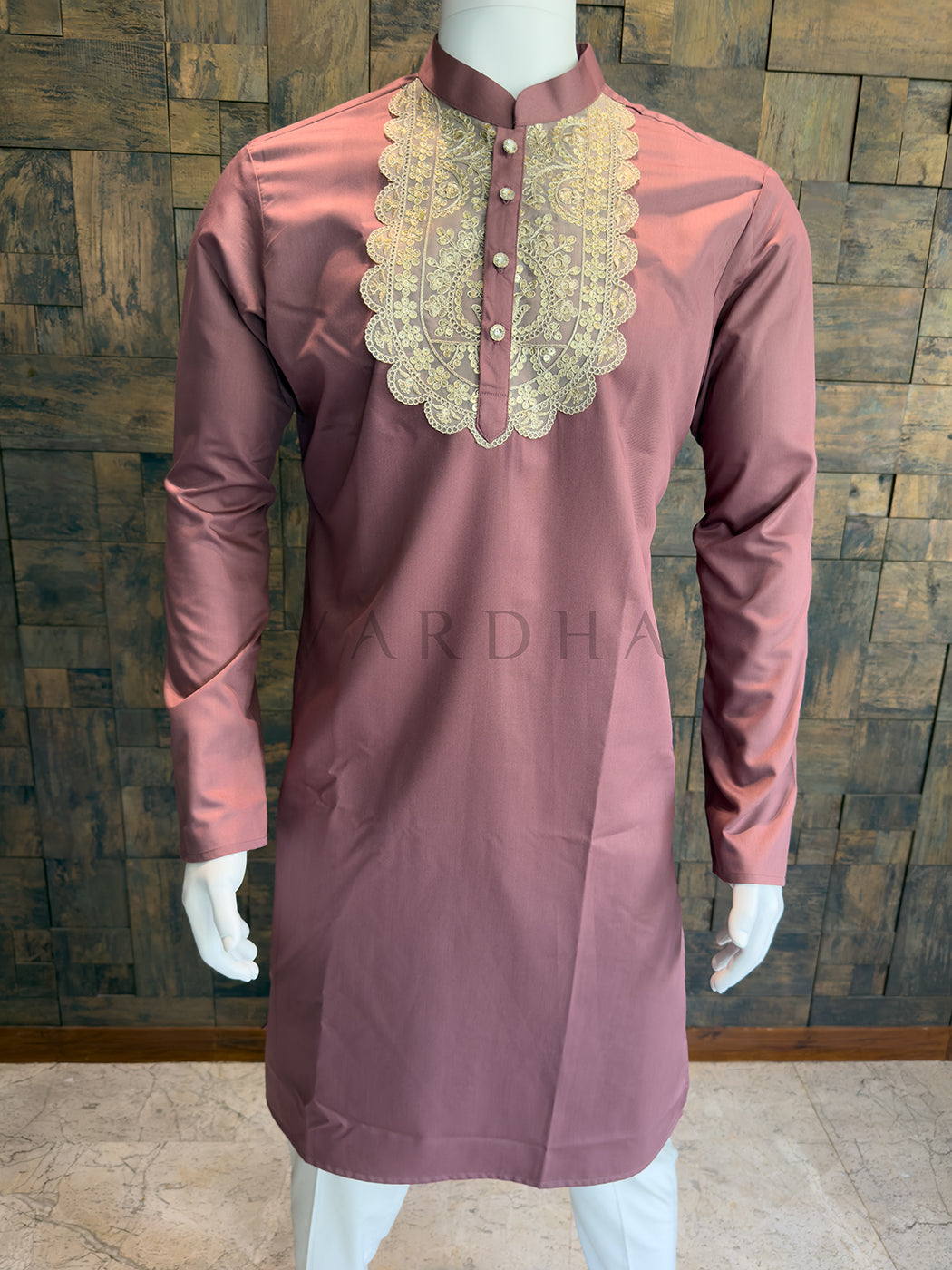 Mauve kurta with gold embroidery on a mannequin against a wooden paneled wall. Elegant dusty pink designer kurta for men, an impeccable choice for Sangeet nights and daytime weddings, featuring a crisp Mandarin collar.