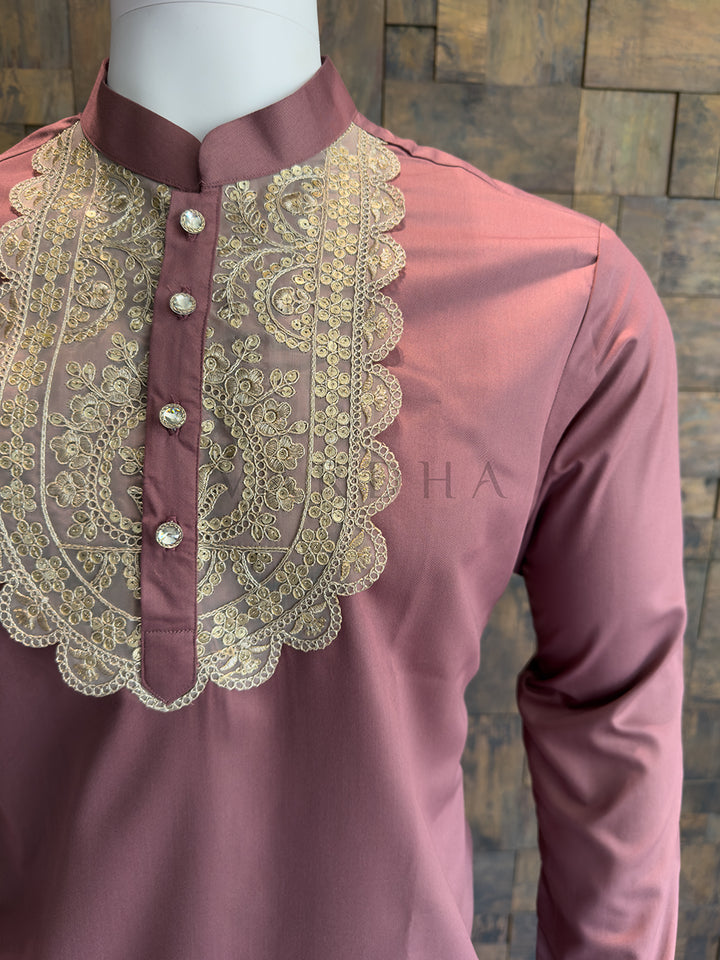 Maroon shirt with gold embroidery on a mannequin against a wooden panel background. Men’s Mauve Pink kurta with an intricately embroidered bib and crystal designer buttons, creating a sharp and luxurious ethnic silhouette.